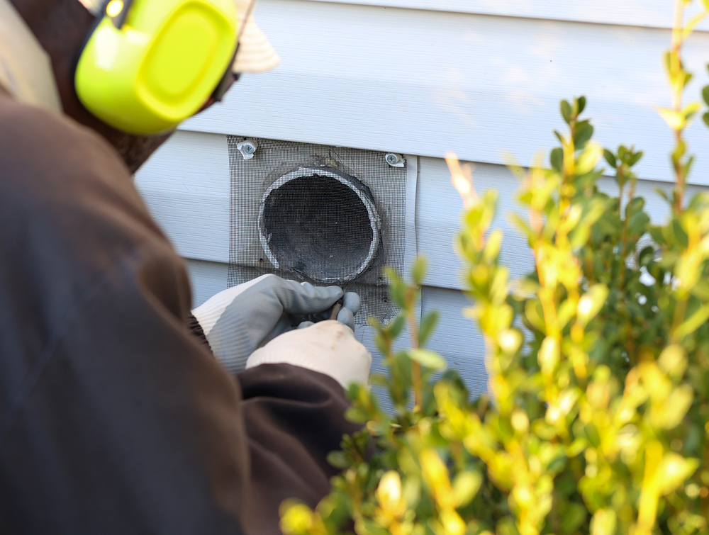 Person cleaning exterior dryer vent opening.