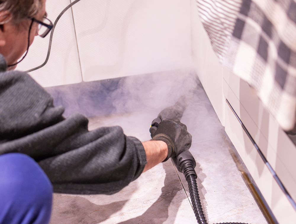 Person steam cleaning floor corner with hose.