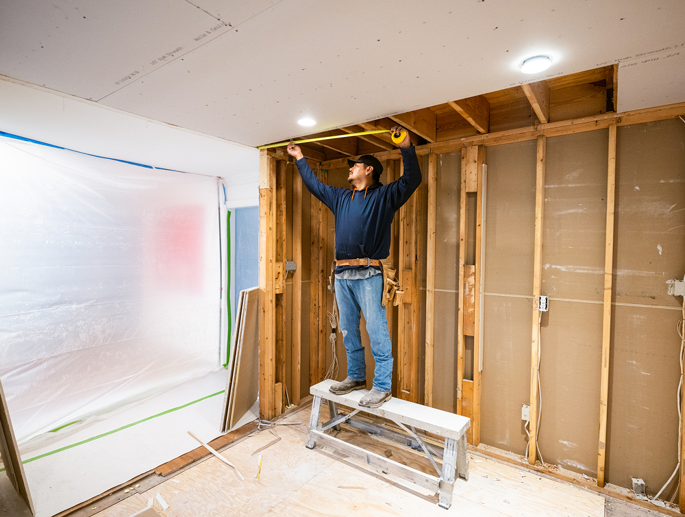 Person measuring ceiling in construction site.